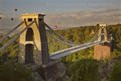 Clifton Suspension Bridge in early morning sunlight, with hot air balloons in the Bristol Balloon Fiesta (August) flying overhead, Clifton, Bristol, Great Britain.