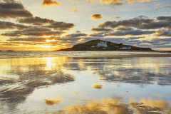 A sunset view across wet sand towards Burgh Island, at Bigbury, Devon, Great Britain.